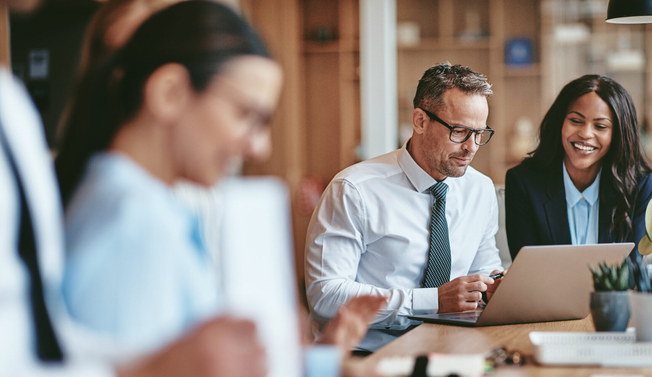 Two diverse businesspeople smiling while working on a laptop together at the end of a boardroom table in an office